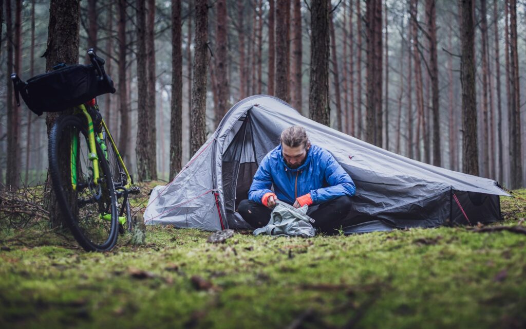 man in blue jacket sitting on green grass field near gray tent during daytime